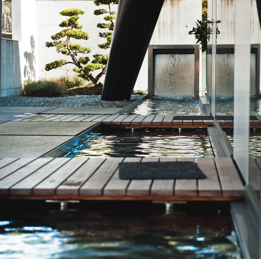 Eingangsbereich mit einer Holzbrücke und Wasser